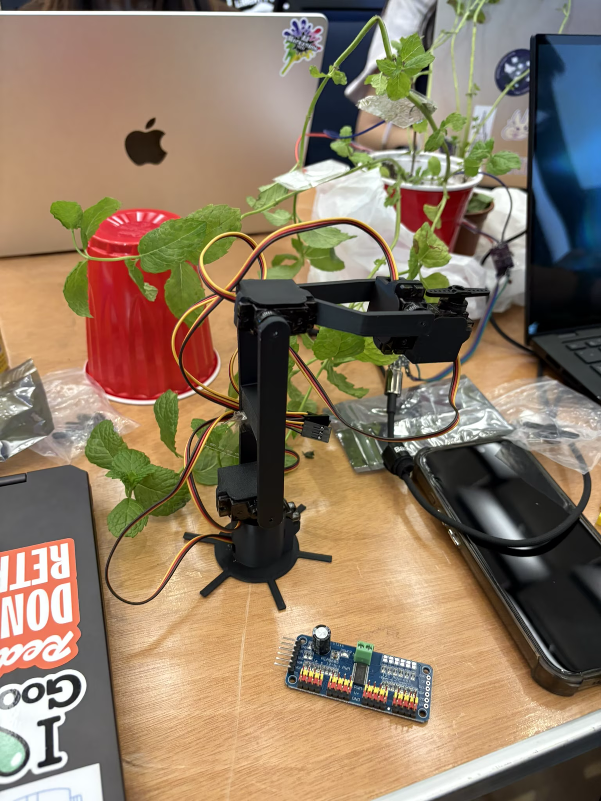 Plantcasso prototype on a table with a mint plant, electronics, and a small robot arm