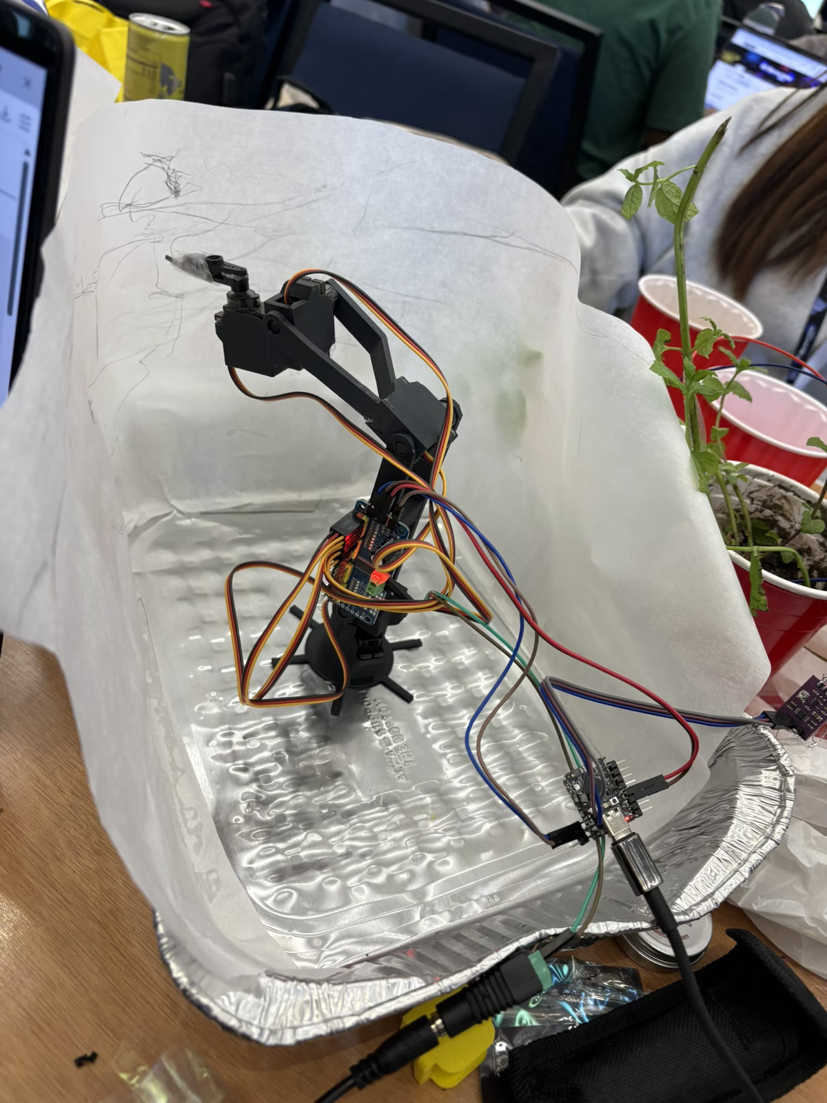 A small robot arm wired inside a foil enclosure with a mint plant beside it